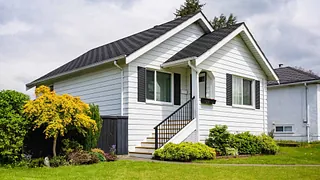 Hvit enebolig med sort tak og velstelt hage foran.