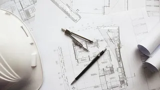 Arkitekttegninger med hjelm, passer og blyant lagt utover bordet.